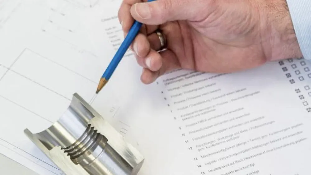 Inspector checking a machined part against an engineering drawing and inspection sheet