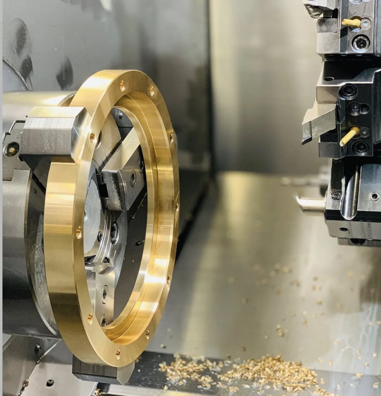 Large brass bearing ring being precision-turned on a multi-axis CNC lathe at Brassland, with brass chips visible — CNC machining of brass
