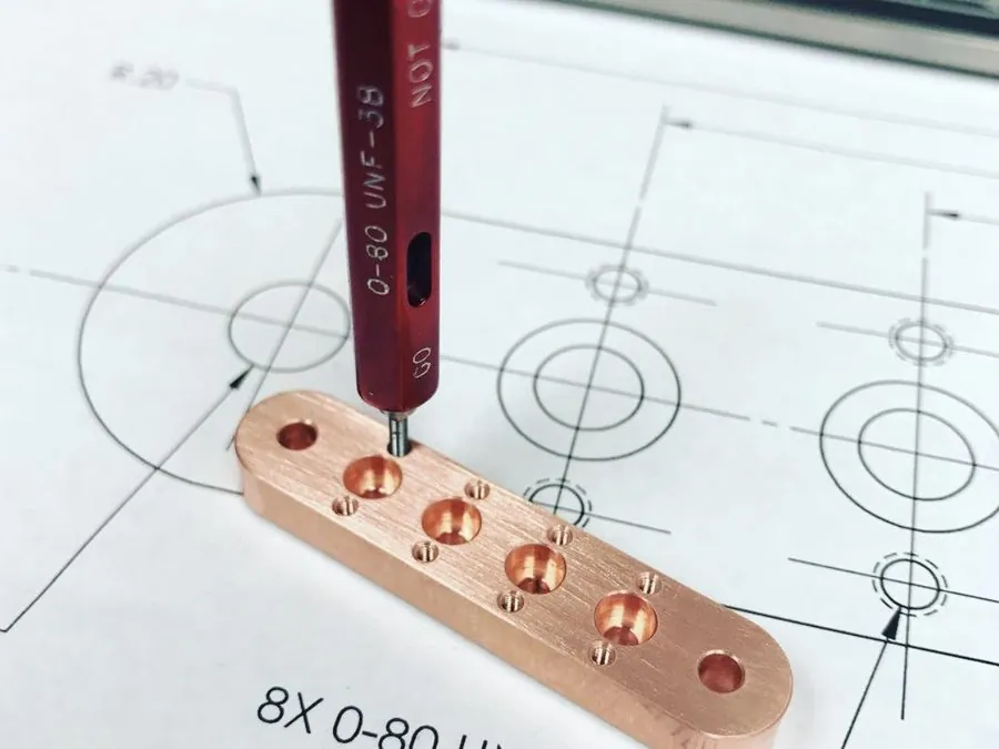 Go/no-go thread plug gauge checking a machined copper part over an engineering drawing at Brassland