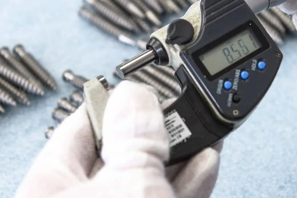 Inspector measuring the diameter of machined threaded studs with a digital micrometer at Brassland